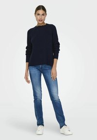 Marineblauer Strickpullover mit Rippstruktur und rundem Ausschnitt, kombiniert mit hellblauen Slim-Fit-Jeans und weißen Sneakers.