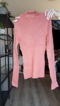 Ribbestrikket langermet topp i myk rosa, med høy hals og tettsittende silhuett, laget av et elastisk materiale for komfortabel bruk.