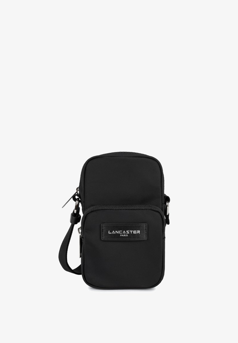 Sac bandoulière en nylon noir avec fermeture éclair, présentant un patch logo à l'avant et une sangle ajustable. Texture lisse, design compact.