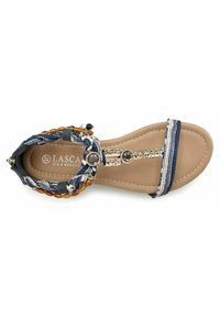 Blaue gemusterte Sandalen mit geflochtenen Riemen, goldenen Akzenten, flacher, brauner Sohle und metallischen Dekorationselementen im Zehenbereich.