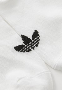 Λευκές κάλτσες με μαύρο κεντημένο λογότυπο που μοιάζει με πεταλούδα και έχει ριγέ λεπτομέρεια στο κέντρο. Βαμβακερή υφή, λεία φινίρισμα.