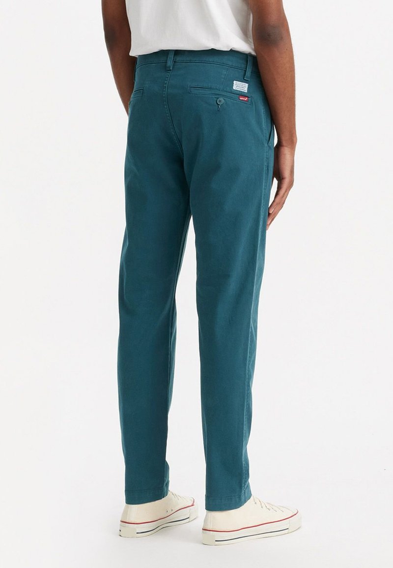 Pantalons en coton turquoise au fit slim, avec des poches au dos et une étiquette de marque rouge sur le côté droit. Fabriqués en tissu lisse avec une apparence soignée.