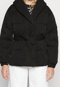 Svart puffjacka med omslag design, överdimensionerad krage, bälte i midjan och elastiska ärmslut. Har en jämn yta och quiltad mönster.