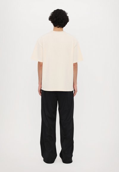 Beige oversized t-skjorte med rund hals, korte ermer og avslappet passform, kombinert med løstsittende svarte bukser.