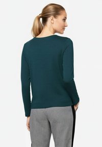 Turquoise long-sleeve top with a round neckline, paired with black and white checkered pants. Smooth fabric and relaxed fit design.