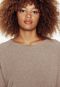 Pullover di colore marrone chiaro, morbido al tatto, con un ampio scollo e maniche raglan, caratterizzato da un delicato motivo melange su tutta la superficie.