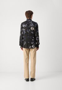 Schwarzes Hemd mit weißem und blauem Rosenmuster, lange Ärmel, mit geknöpften Manschetten. Kombiniert mit beigen Hosen und schwarzen Schuhen.