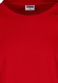 Tricou sportiv roșu din plasă, cu guler rotund, având o etichetă pe care scrie "URBAN CLASSICS M" cosută în interior. Textură ușoară și respirabilă.