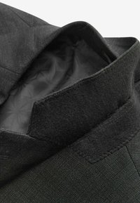 Der Kragen der schwarzen Jacke zeigt einen strukturierten Stoff und ein glattes Innenfutter mit geometrischem Muster; an der Kante befindet sich ein Wollakzent.
