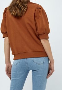 Brown pullover sweatshirt with puffed sleeves and ribbed hem, paired with light blue fitted jeans. Smooth texture, casual design.