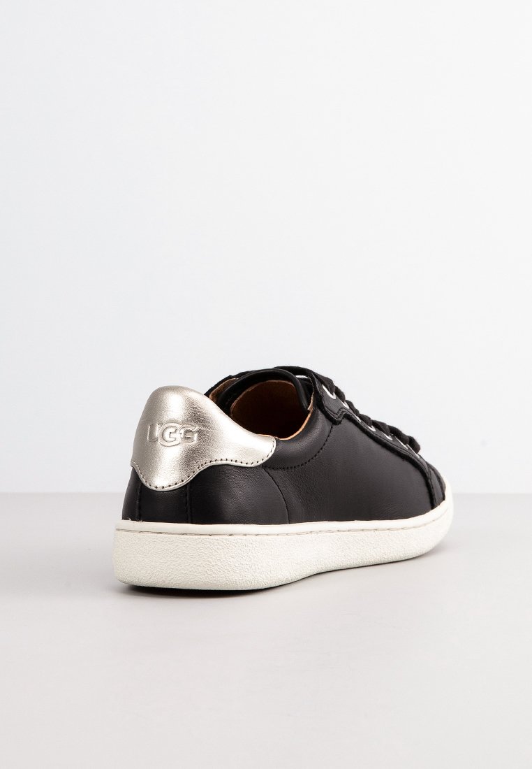 Zapatilla negra de cuero con un acento metálico plateado en el talón, cordones texturizados y suela de goma blanca. Logo situado en el talón.