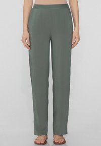 Pantaloni ampi in verde tenue, realizzati in tessuto leggero. Presentano una cintura liscia e un taglio dritto, abbinati a sandali semplici.