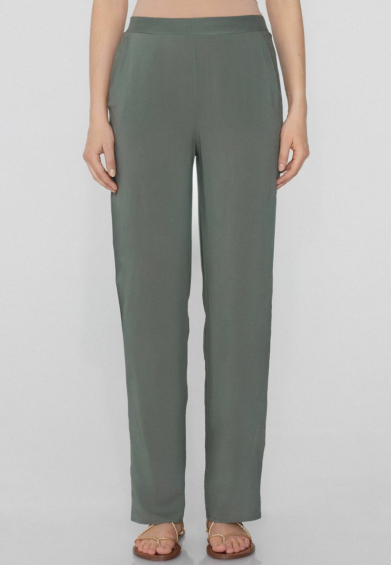 Pantaloni ampi in verde tenue, realizzati in tessuto leggero. Presentano una cintura liscia e un taglio dritto, abbinati a sandali semplici.