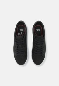 Ein Paar schwarze Schnürsneaker mit weißen Sohlen, von oben auf einem weißen Hintergrund fotografiert.