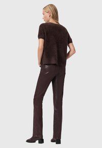 Maglione marrone in maglia pelosa con maniche corte e vestibilità comoda, abbinato a pantaloni aderenti in pelle marrone scuro e stivaletti con tacco.