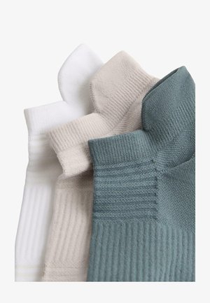 Három pár bordázott bokazokni fehér, bézs és matt zöld színekben, egymáson átfedésben elrendezve fehér háttéren.