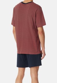 Kurzes rotes T-Shirt mit gemustertem Textur und marineblauen Akzenten, kombiniert mit marineblauen Shorts, die ein lässiges Outfit schaffen.