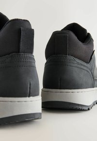 Mustat lenkkarit, jotka on valmistettu sileistä ja teksturoiduista materiaaleista, harmaan pohjan ja pehmustetun varren kanssa. Suunnittelussa on tyylikäs, pyöreä muoto.