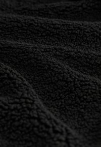 Černá fleecová látka s měkkým, texturovaným povrchem, který má nadýchaný a nepravidelný vzor, zdůrazňující její teplo a pohodlí.