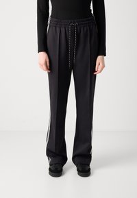 Pantalons de sport noirs en tissu texturé, dotés d'une taille élastique avec cordon de serrage, de bandes blanches sur les côtés et d'une coupe décontractée.