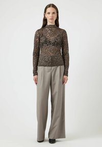 Blondtopp i mørk brun med blomsterpattern, høy hals og lange ermer, kombinert med rette, lysegrå bukser. Svarte sko.