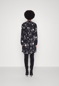 Musta mekko, jossa on valkoisia tähden kuvioita, pitkät hihat ja röyhelöhelma, yhdistettynä mustiin kimaltaviin polven korkeisiin saappaisiin.