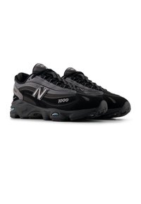 Μαύρα και γκρι αθλητικά παπούτσια με δίχτυ και συνθετικά υλικά, μεγάλο πάτο, ασημί λεπτομέρειες και εμφανές λογότυπο "N".