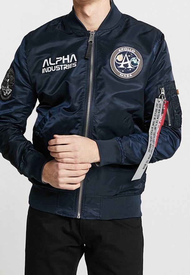 Chaqueta bomber azul marino hecha de nylon brillante. Cuenta con cremallera frontal, parche en el pecho, logo y etiqueta roja en la manga. Puños y cintura acanalados.