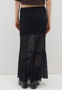 Schwarzer Spitzen-Maxi-Rock mit geschichteten durchsichtigen Abschnitten, gewellten Säumen und strukturierten Mustern. Elastischer Bund und knöchellanges Design.