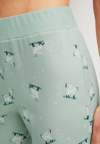 Lichtgroene leggings met een speels patroon van witte geiten op ski's, met zwarte accenten en een geribde tailleband.