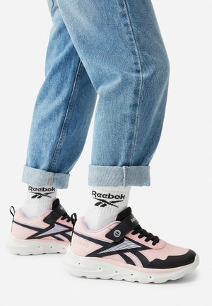 Nohy v růžovo-černých teniskách Reebok se bílými ponožkami Reebok, v kombinaci s ohrnutými světle modrými džíny.