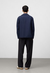 Granatowa kurtka o gładkiej fakturze, z pełnymi rękawami i klasycznym kołnierzykiem. Czarne spodnie z szerokimi nogawkami i beżowe buty z zielonymi akcentami.