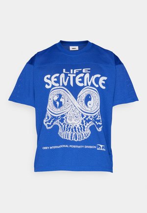 T-shirt bleu en maille à manches courtes présentant un design graphique blanc d'un crâne avec des détails complexes et le texte "LIFE SENTENCE" en dessous.