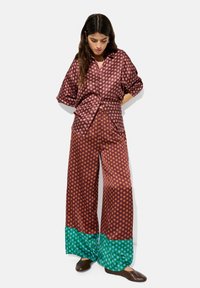 Sukienka satynowa z fioletowo-brązowym wzorem w kropki, szerokie spodnie z zielonym akcentem na końcu nogawek oraz luźna koszula zapinana na guziki.