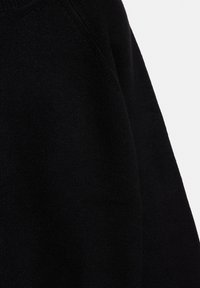 Musta neulottu neuletakki, jossa on teksturoitu pinta, pyöreä kaula-aukko ja raglan-hiha-tyyli. Yksityiskohtiin kuuluu hienovarainen resorikuvio reunojen ympärillä.