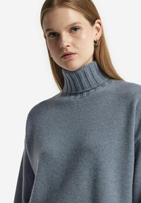 Niebieski sweter dzianinowy z wysokim prążkowanym kołnierzem, o miękkiej fakturze i luźnym kroju. Minimalistyczny design bez wyraźnych wzorów czy akcentów.