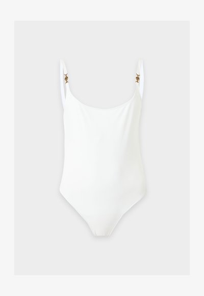 Maillot de bain une pièce blanc avec fines bretelles réglables et petites attaches décoratives dorées sur un fond clair.