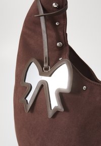 Sac à main en daim marron avec un grand nœud miroir et des clous argentés le long du bord supérieur, doté d'une bandoulière incurvée.