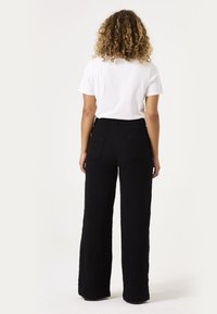 Zwarte wijde broek met achterzakken, gemaakt van een textuurstof. Gecombineerd met een eenvoudige witte T-shirt. Focus op een eenvoudig, functioneel ontwerp.