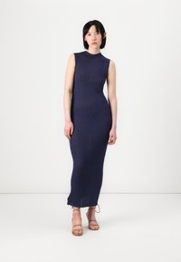 Rochie fără mâneci de culoare bleumarin, cu o siluetă ajustată și țesătură texturată. Croială până la gleznă, cu o ușoară uzură la margine.