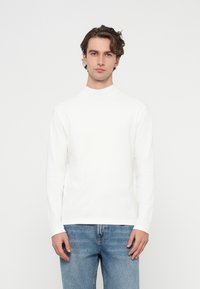 Biała koszula z długim rękawem i wysokim kołnierzem, wykonana z miękkiej bawełny, zestawiona z jasnoniebieskimi dżinsami. Prosty krój i dopasowany fason.