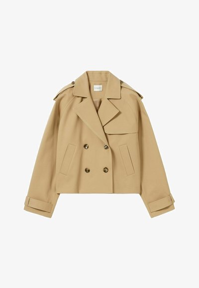 Cappotto trench corto beige con design doppiopetto, ampie tasche frontali e spalle strutturate. Presenta bottoni dorati e cinturini sui polsini.