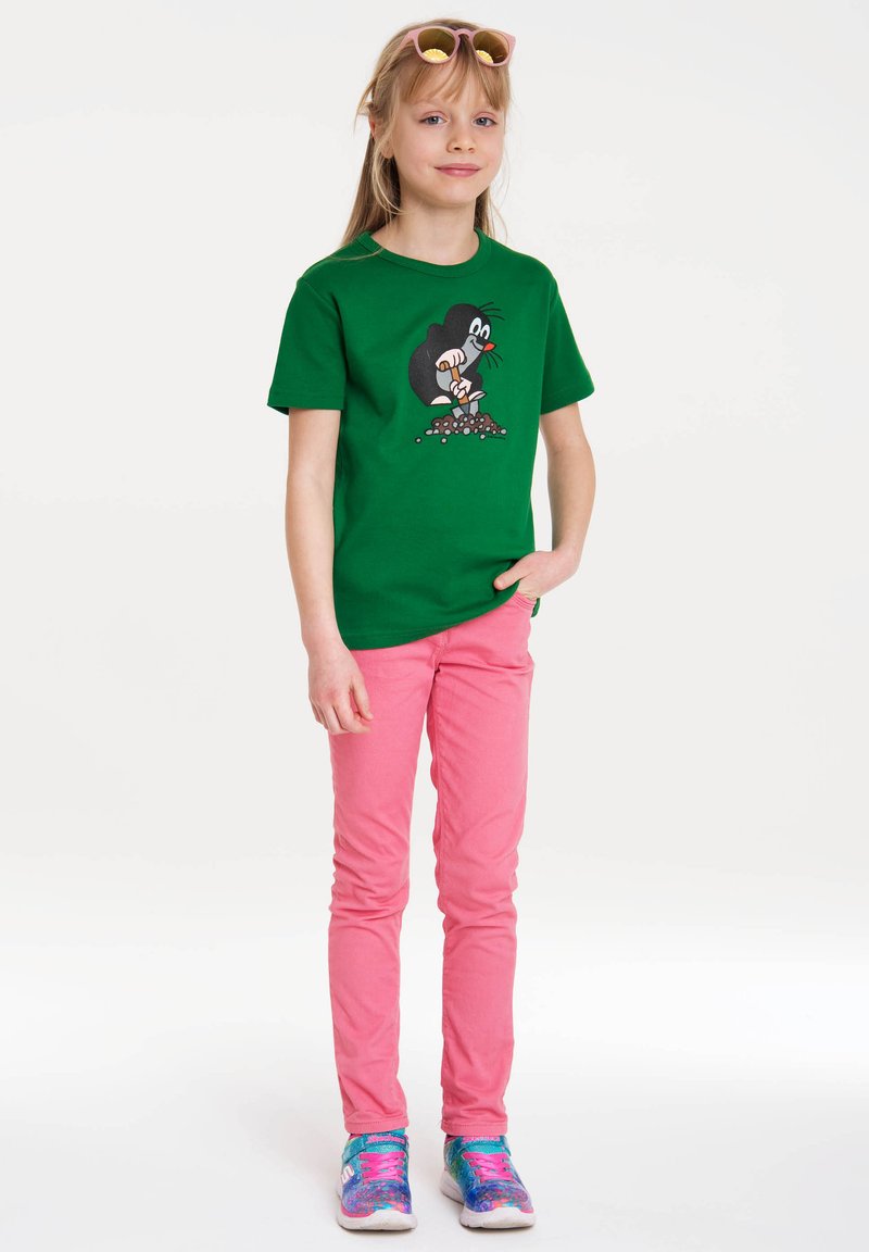 Green cotton T-shirt featuring a cartoon character graphic on the front, paired with pink skinny jeans and multicolored athletic shoes.