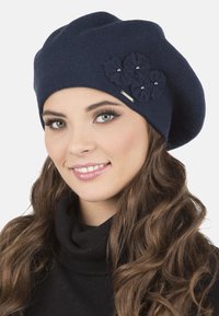 Beret lavorato a maglia navy con tre fiori in tessuto texture, accentuato da piccole perle e un'etichetta metallica. Texture morbida e liscia.
