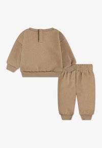 Ruskea puuvillasekoitteinen verryttelypuku, jossa on pyöreäkauluksinen pusero resorireunuksilla sekä siihen sopivat kapealahkeiset housut joustavalla vyötäröllä.