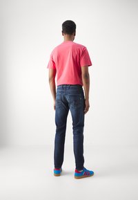 Röd bomull t-shirt i kombination med mörkblå jeans. Skorna har blå och röda accenter, med en mockaliknande textur och gummisålar.