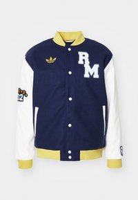 Granatowa kurtka varsity z białymi rękawami, żółtym kołnierzem i mankietami, zapięciem na zatrzaski oraz naszywkami, w tym "RM" i logo Adidas.