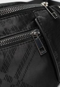 Black fabric bag featuring multiple zippered compartments, sleek metallic hardware, and a textured pattern embossed on the surface.