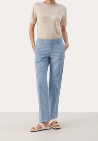  Lichtblauwe katoenen broeken met een relaxed fit, zijzakken en een gladde textuur. Gecombineerd met een beige top met korte mouwen en sandalen.