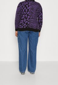 Schwarzer und lila gestrickter Pullover mit Tiermuster und geripptem Saum, kombiniert mit hellblauen weit geschnittenen Jeans und schwarzen Schuhen.